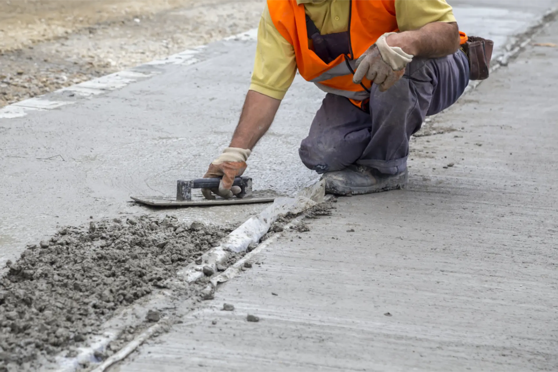 A concreter kneeling to trowel the joint line of a freshly poured concrete slab