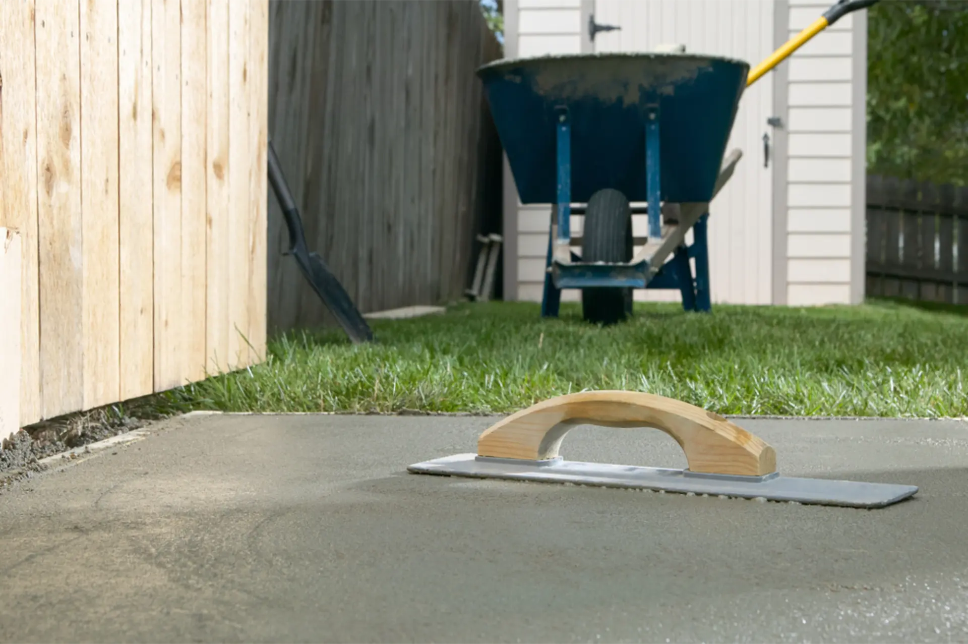 A wheelbarrow and shovel resting beside a freshly finished backyard slab