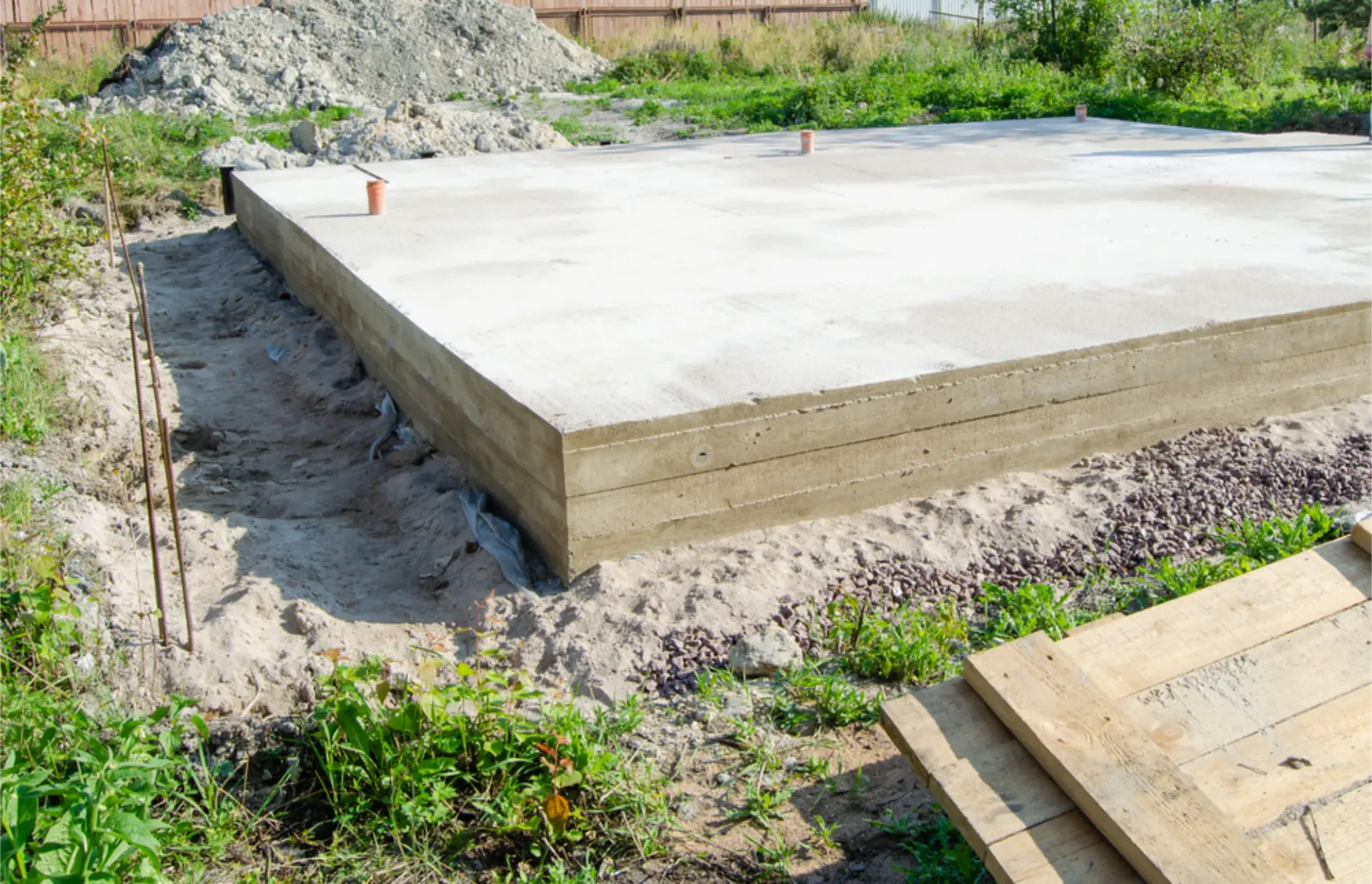 A large poured concrete house slab foundation with formwork edges and plumbing stubs