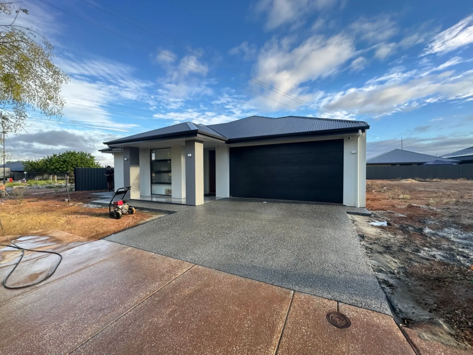 A new concrete driveway running up to a dark garage door with red dirt either side