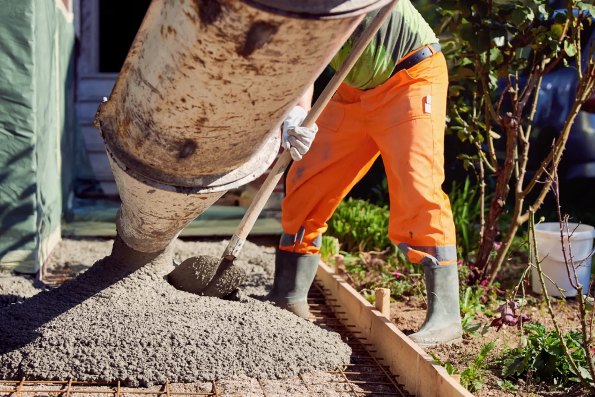 Concrete running down a mixer chute onto reinforcing mesh as a concreter spreads it into timber formwork for a garden path
