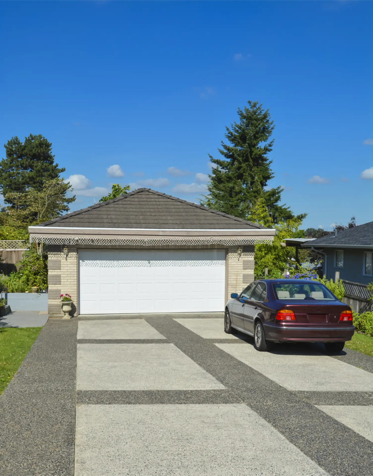A wide concrete driveway to a double garage with a sedan parked on it