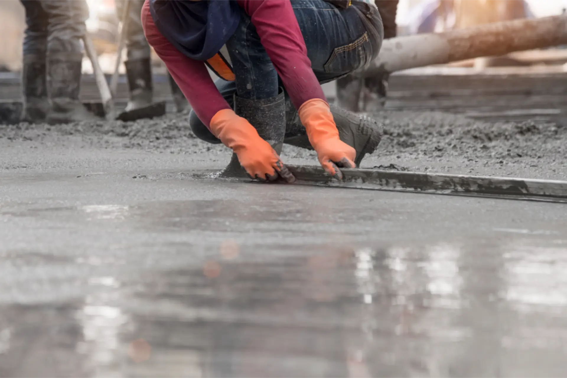 Orange-gloved hands running an edging tool along fresh concrete