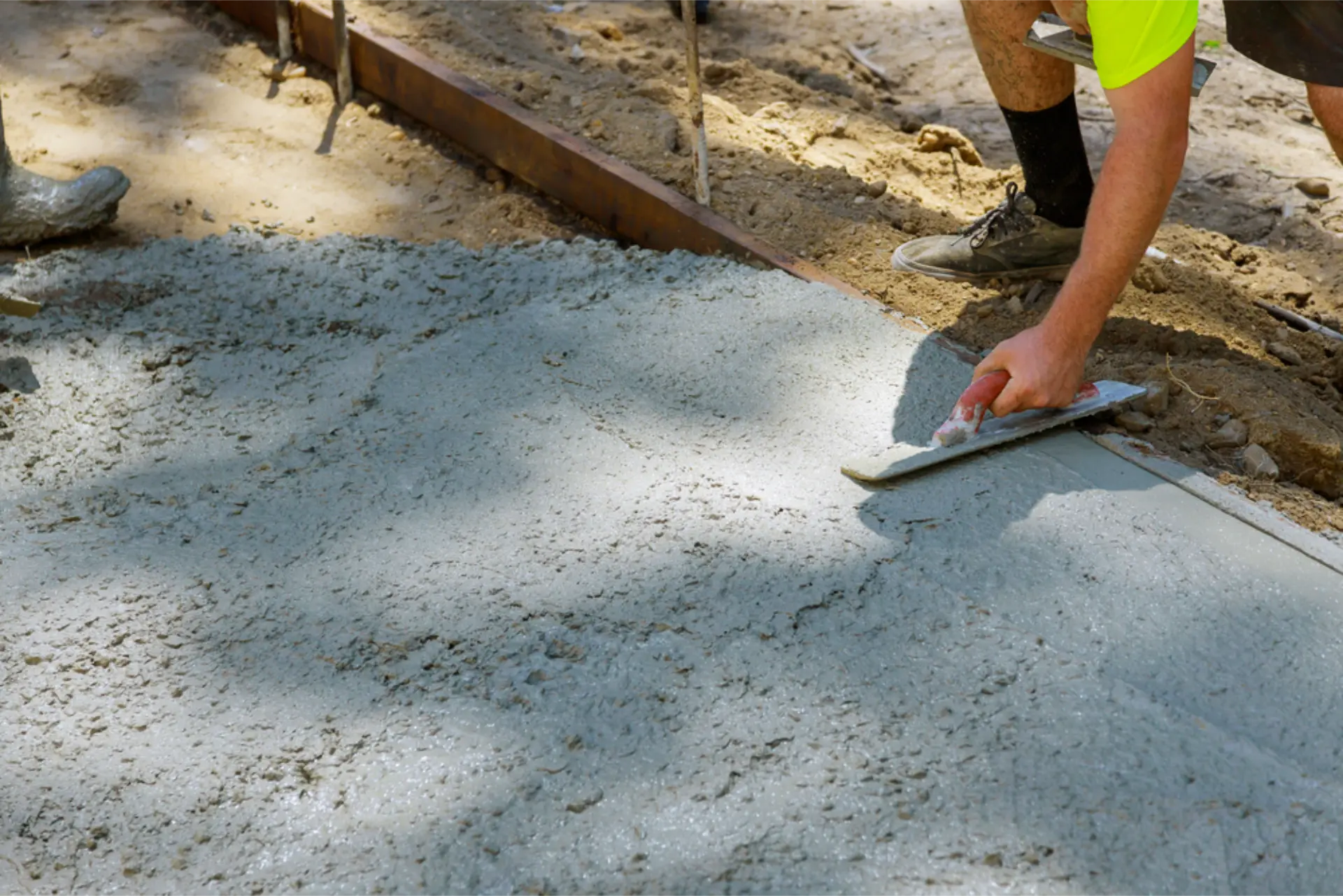 A concreter kneeling to edge-trowel the side of a fresh driveway strip