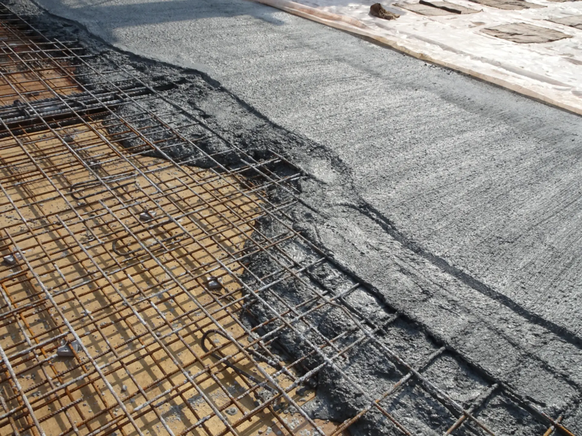 Close-up of wet concrete filling the edge of a slab over reinforcing mesh