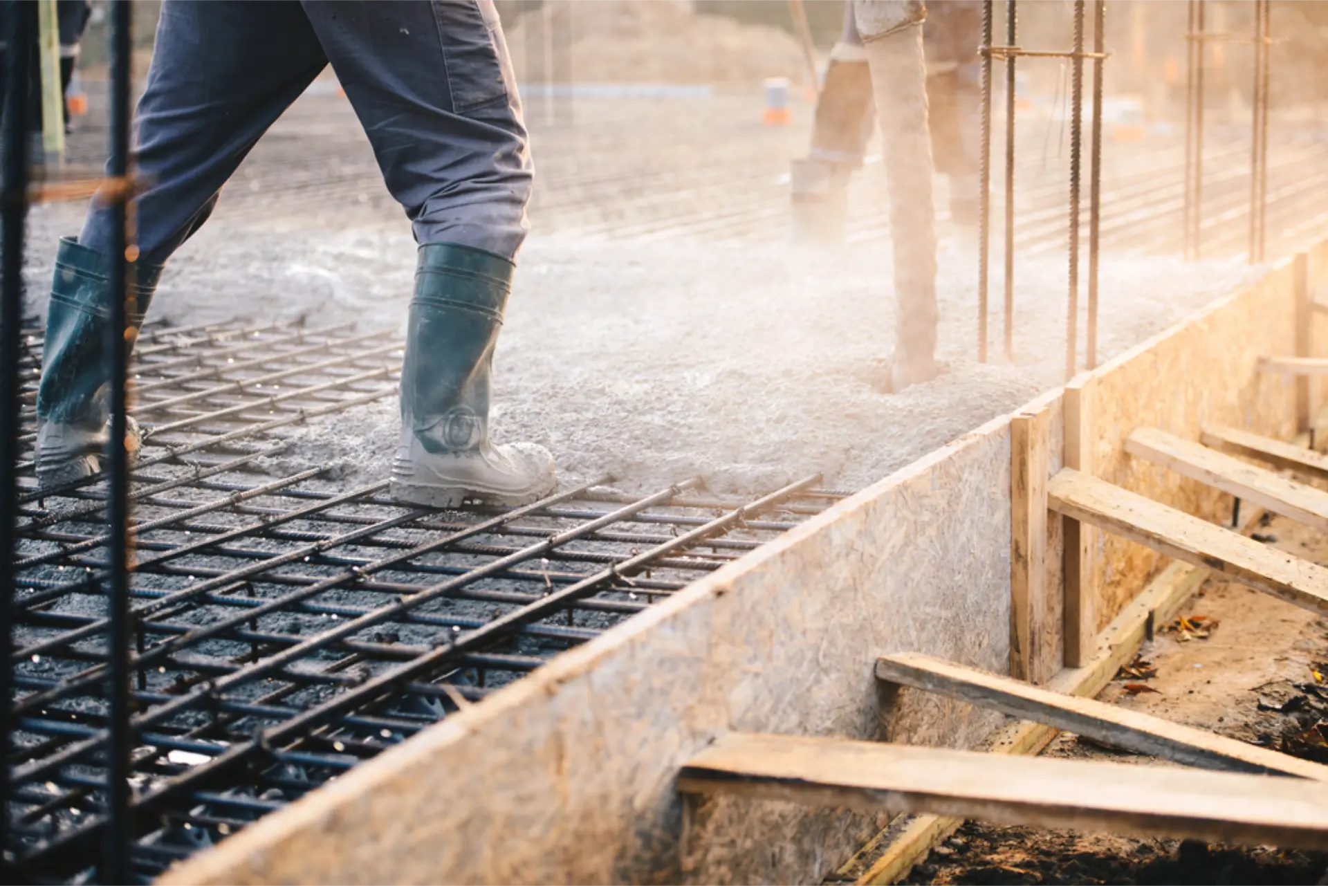 Workers walking across steel reinforcing mesh laid out over a house foundation before the pour